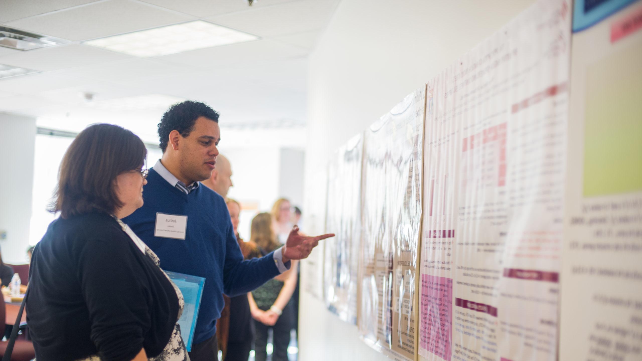 Two professionals looking and discussing material hanging on walls during a linguistics second language conference.