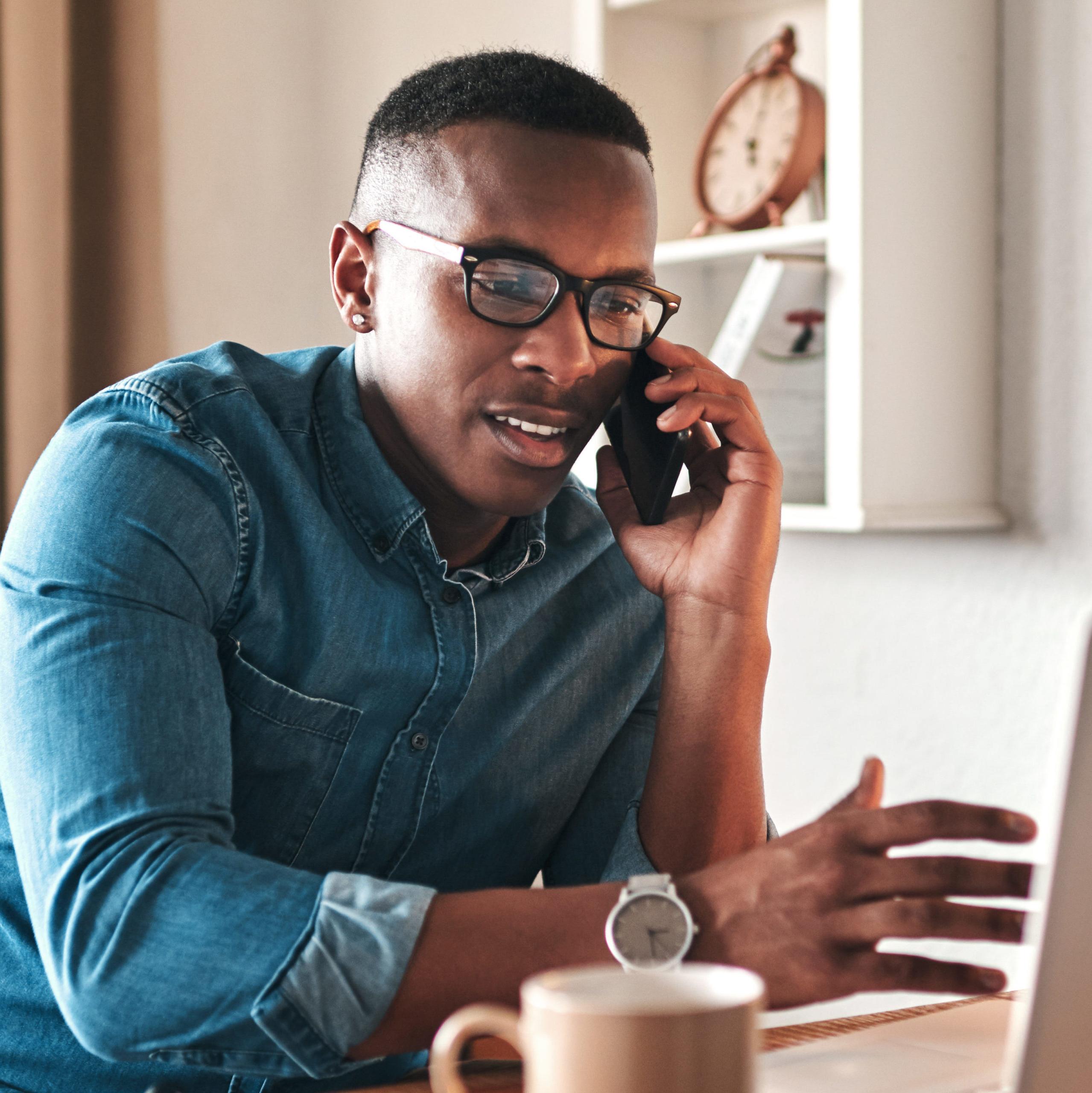 Young businessman sitting down in front of a computer talking on the cellphone.