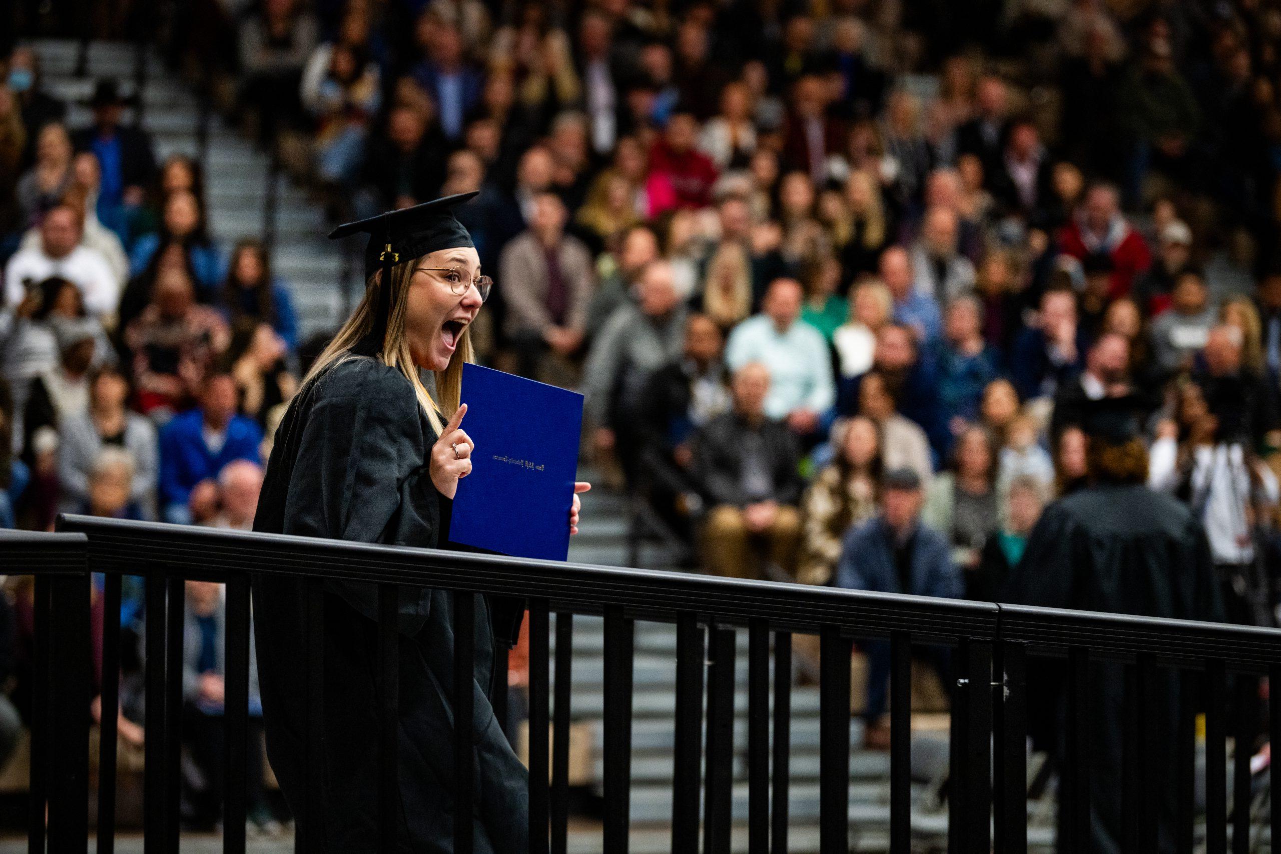 A female student holding her certificate to the rest of the graduates.